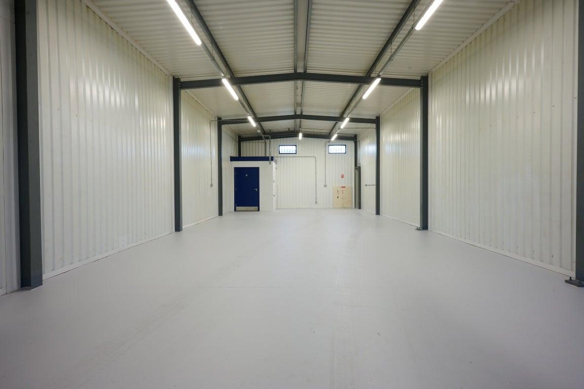 The interior of a warehouse unit, facing the front electric roller shutter, which is closed and large enough for vehicle access.