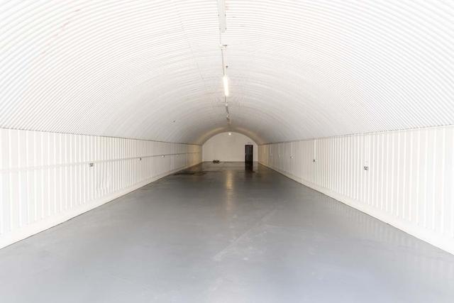 An empty arch with white lining, facing the front electric roller shutter entrance, which is open.