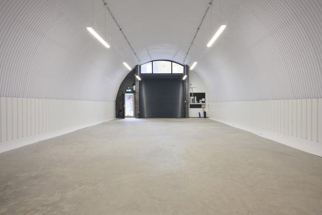 An empty arch with white lining, facing the front electric roller shutter entrance, which is closed.