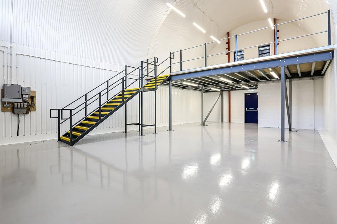 An arch with white lining and a ground floor level and a mezzanine level, connected by stairs.