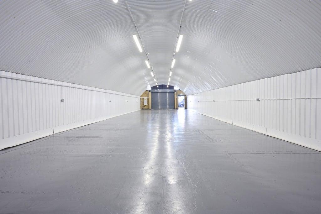 An empty arch with white lining, facing the front electric roller shutter entrance, which is closed.